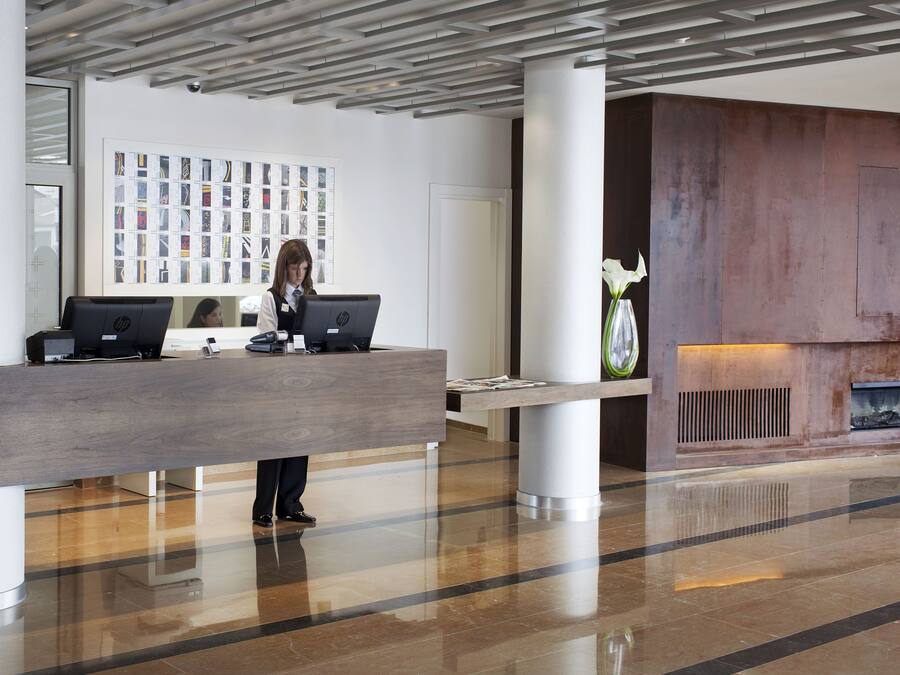A modern reception area with a wooden reception desk, two HP computers, a large wall of photographs, and a decorative vase with a white flower.