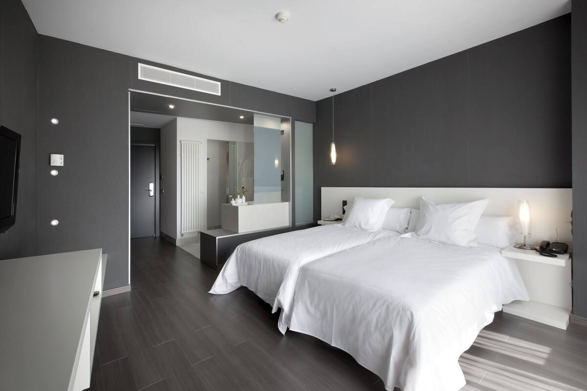 A modern bedroom with a large bed, bedside tables, a mirror, and a walk-in closet.
