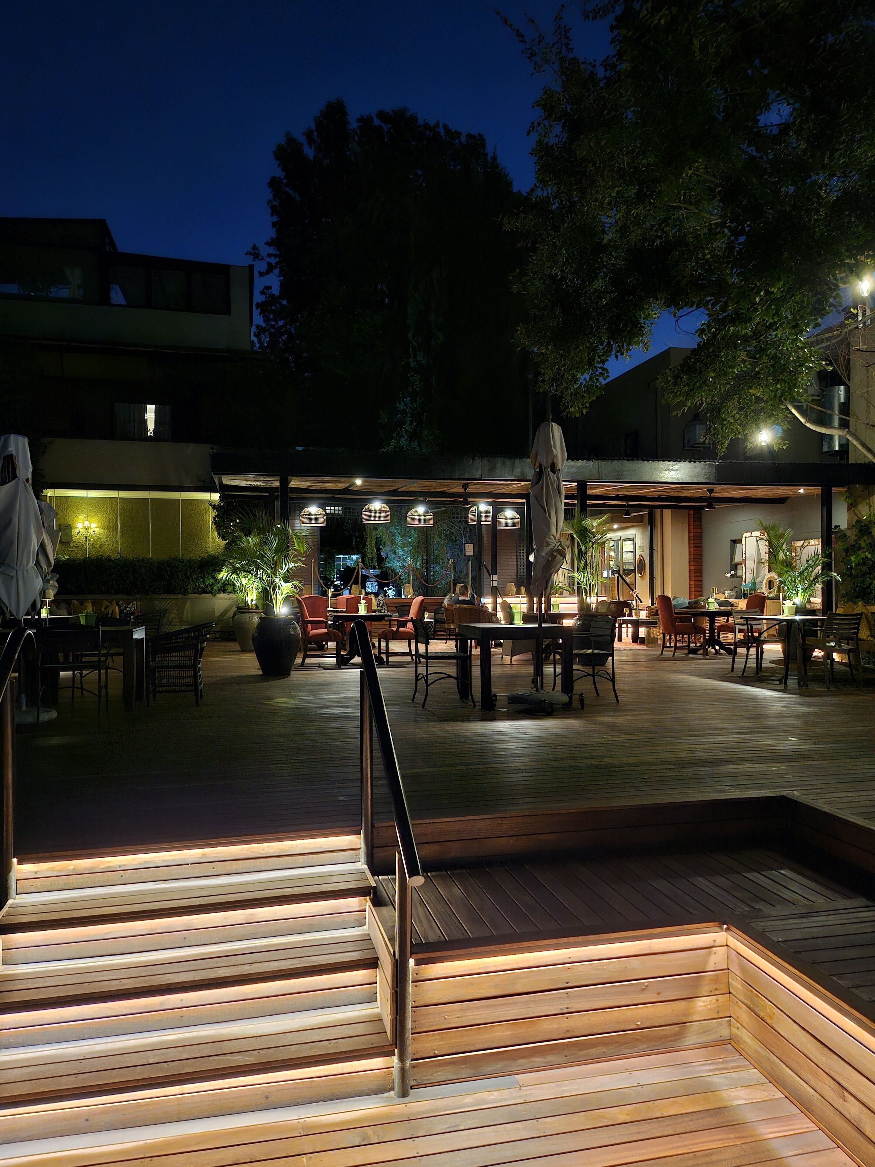An outdoor patio area with wooden flooring, outdoor seating, and ambient lighting.