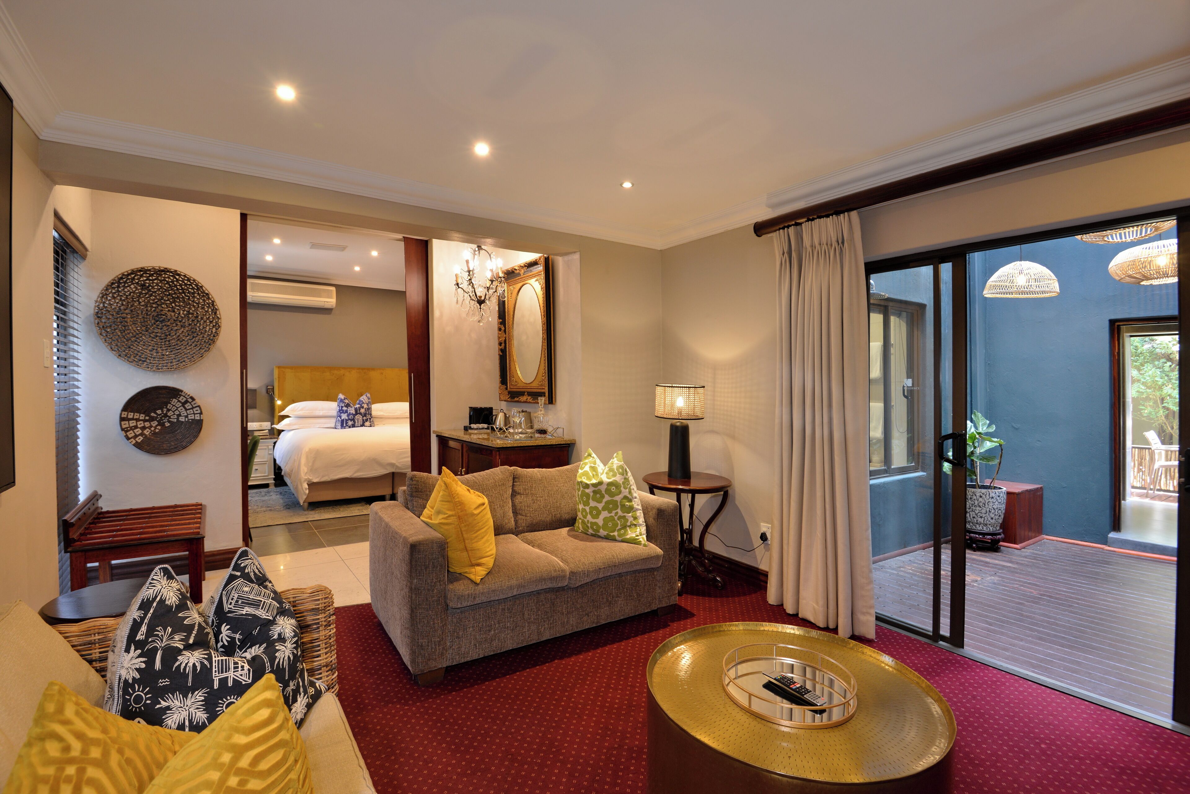 Habitación de hotel con sofá, mesa de centro, cama, espejo y vistas al exterior.