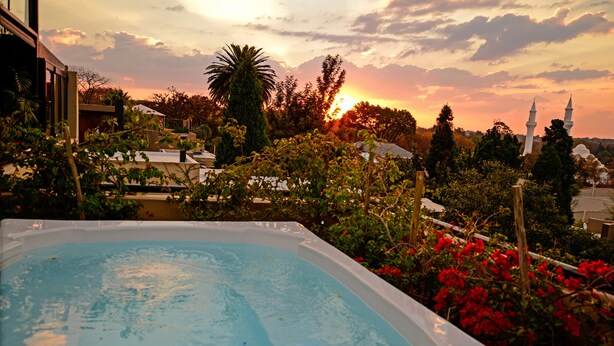 A swimming pool with a sunset view, surrounded by lush greenery and a mosque in the background. - The Residence Boutique Hotel (Johannesburg)