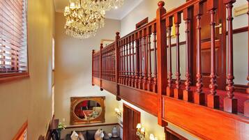 A grand staircase with a chandelier, wooden railings, and a red carpet.