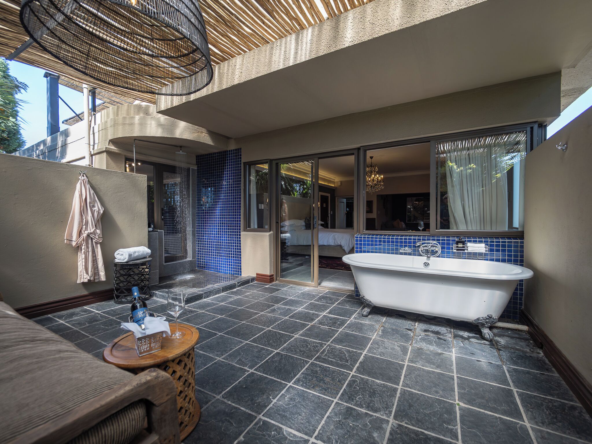A modern bathroom with a freestanding bathtub, a glass-enclosed shower, and a seating area with a small table and a bottle of shampoo.