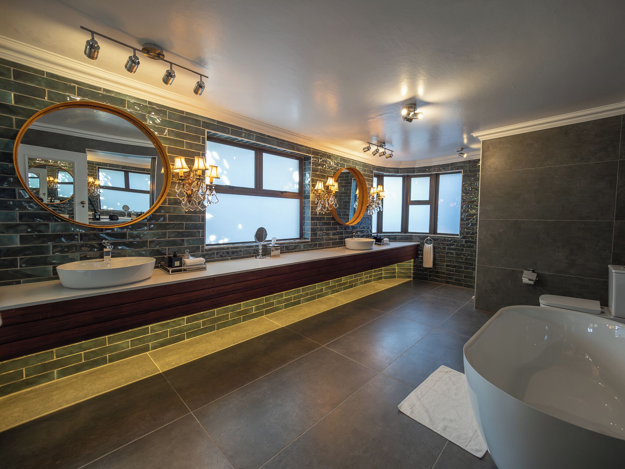A modern bathroom with a large bathtub, two sinks with round mirrors, and a chandelier.