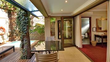 A sunlit patio with a pool, a table, and chairs, leading to a bathroom with a shower and a mirror.