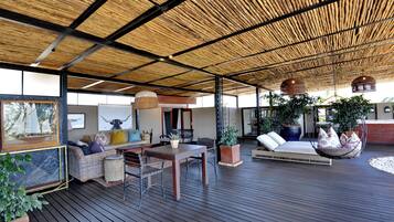 Un amplio espacio al aire libre con una terraza de madera, una mesa de comedor, sillas, un sofá y plantas colgantes.