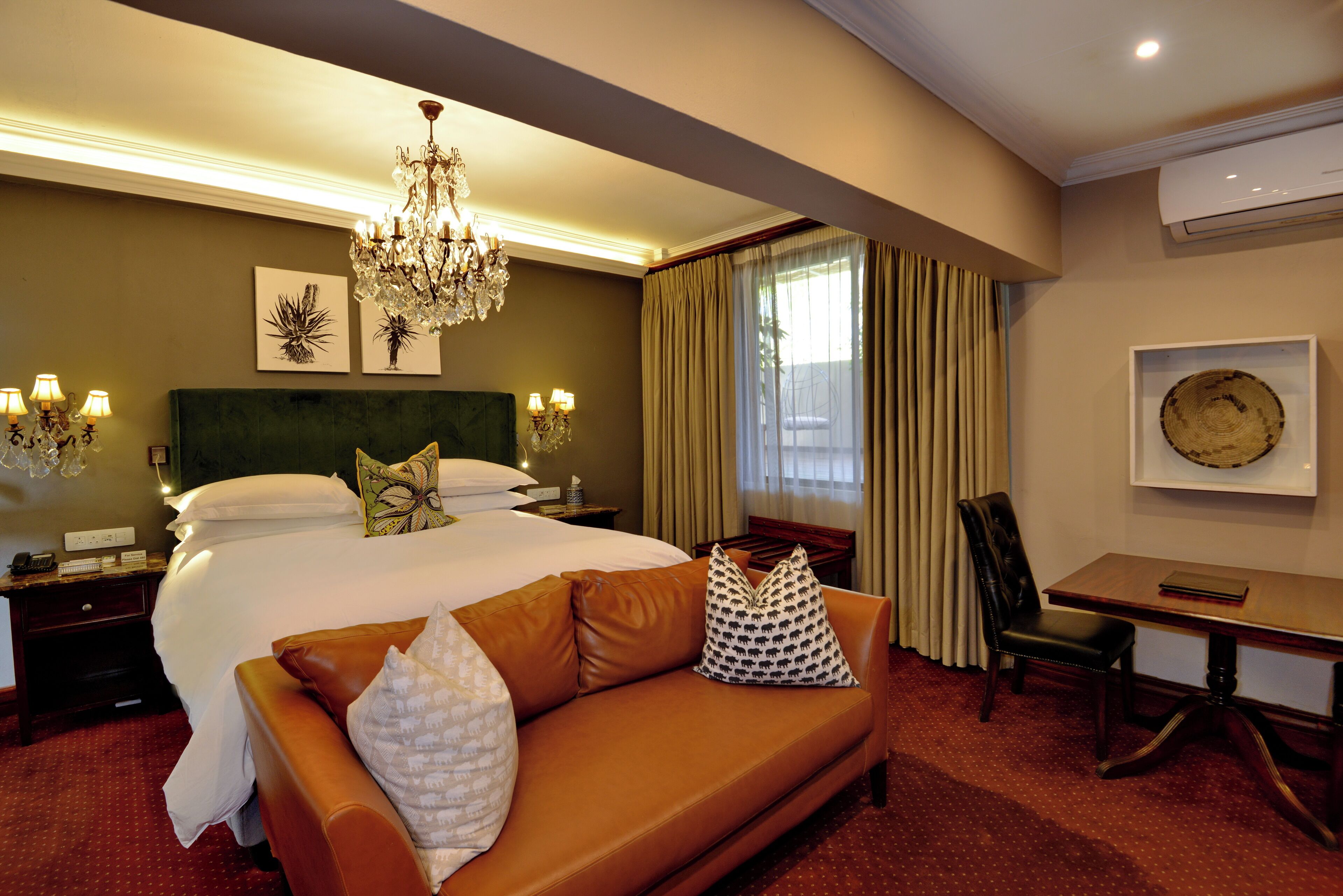 A hotel room with a large bed, a sofa, a desk, and a chandelier.