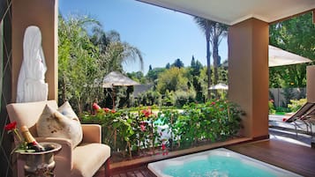 Habitación con vista a un jardín, jacuzzi y zona de estar con sombrillas.