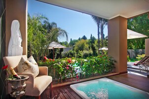 Habitación con vista a un jardín, jacuzzi y zona de estar con sombrillas.