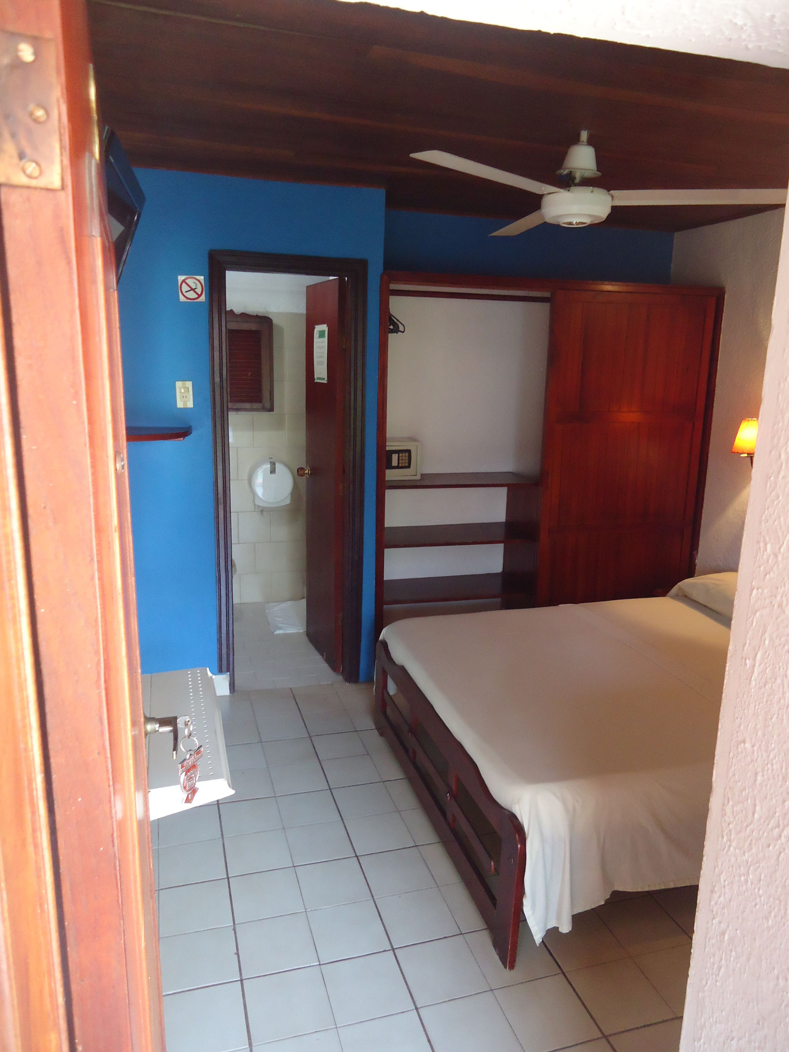 A bedroom with a bed, a ceiling fan, a wooden wardrobe, and a bathroom visible through an open door.