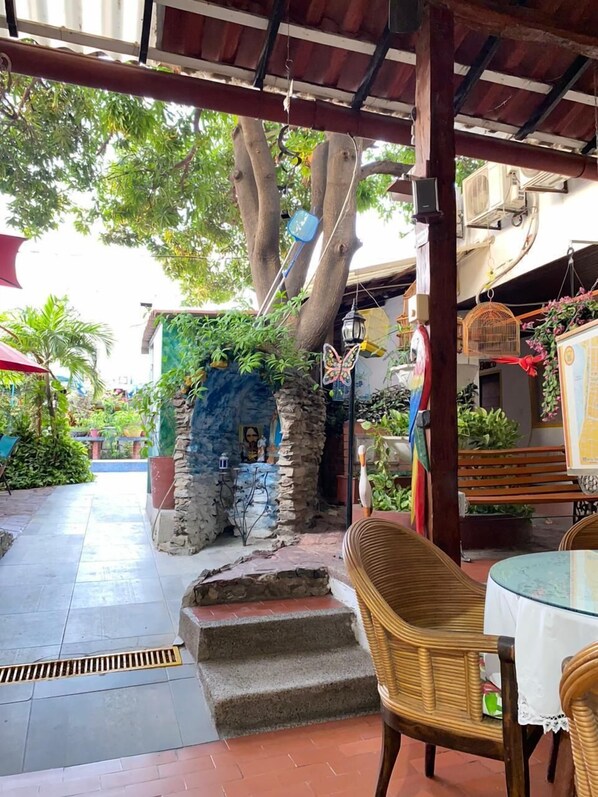 An outdoor patio area with a stone wall, a tree, and a wicker chair. - Hotel Nueva Granada (Santa Marta)