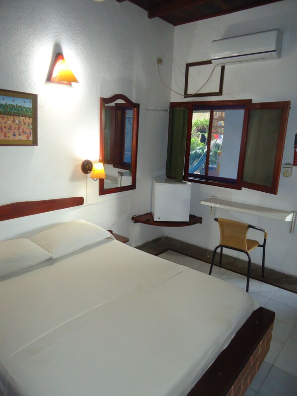 A bedroom with a bed, a desk, a chair, a mirror, and an air conditioning unit. - Hotel Nueva Granada (Santa Marta)