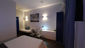 Una habitación pequeña y funcional con cama, escritorio y silla. Hay un cuadro en la pared y una ventana con cortinas.