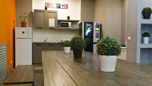 Una cocina moderna con armarios de madera, un refrigerador blanco, un microondas y un refrigerador negro. Hay plantas en macetas sobre la encimera y un letrero que dice "COFFEE".