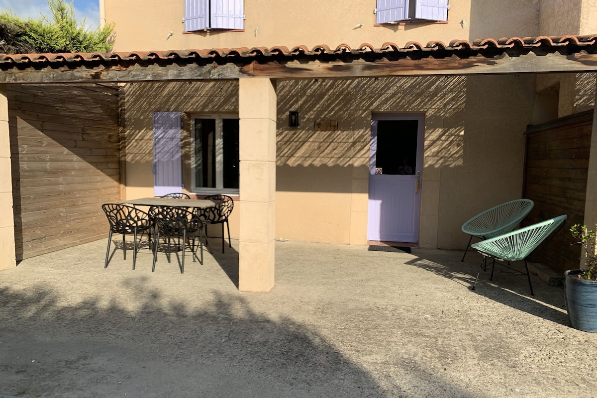 A covered patio area with a table and chairs, a door, and a potted plant.
