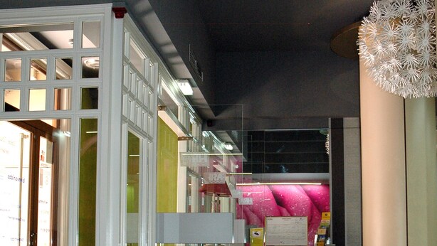 Un moderno vestíbulo de hotel con una recepción, un separador de vidrio y una lámpara decorativa en el techo.