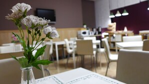 Un restaurante con mesas y sillas blancas, un jarrón con flores y un televisor en la pared.