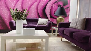 Una sala de estar moderna con un sofá morado, una mesa de centro blanca, un jarrón con flores y un gran mural floral rosa en la pared.