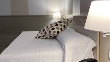 Habitación de hotel con una cama, almohadas, una lámpara de noche y un teléfono sobre una mesita.