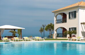 Área da piscina com espreguiçadeiras e um espaço coberto para sentar, com vista para um corpo de água.