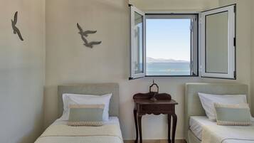 Quarto com duas camas, janela com veneziana aberta e vista para o mar.