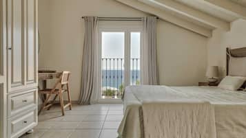 Een slaapkamer met een bed, een bureau en een stoel. Er is een balkon met uitzicht op zee.