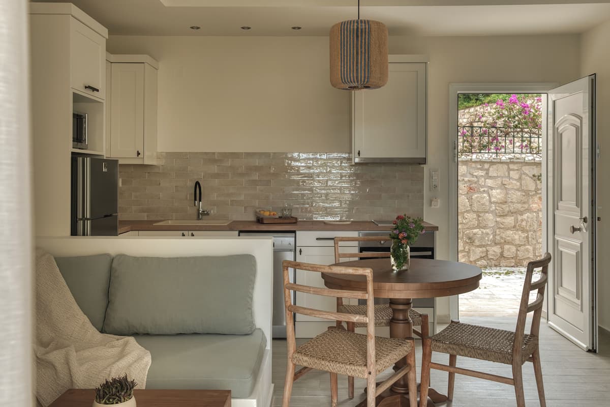 A modern kitchen with white cabinets, a brick backsplash, and a dining area with a round table and wicker chairs.