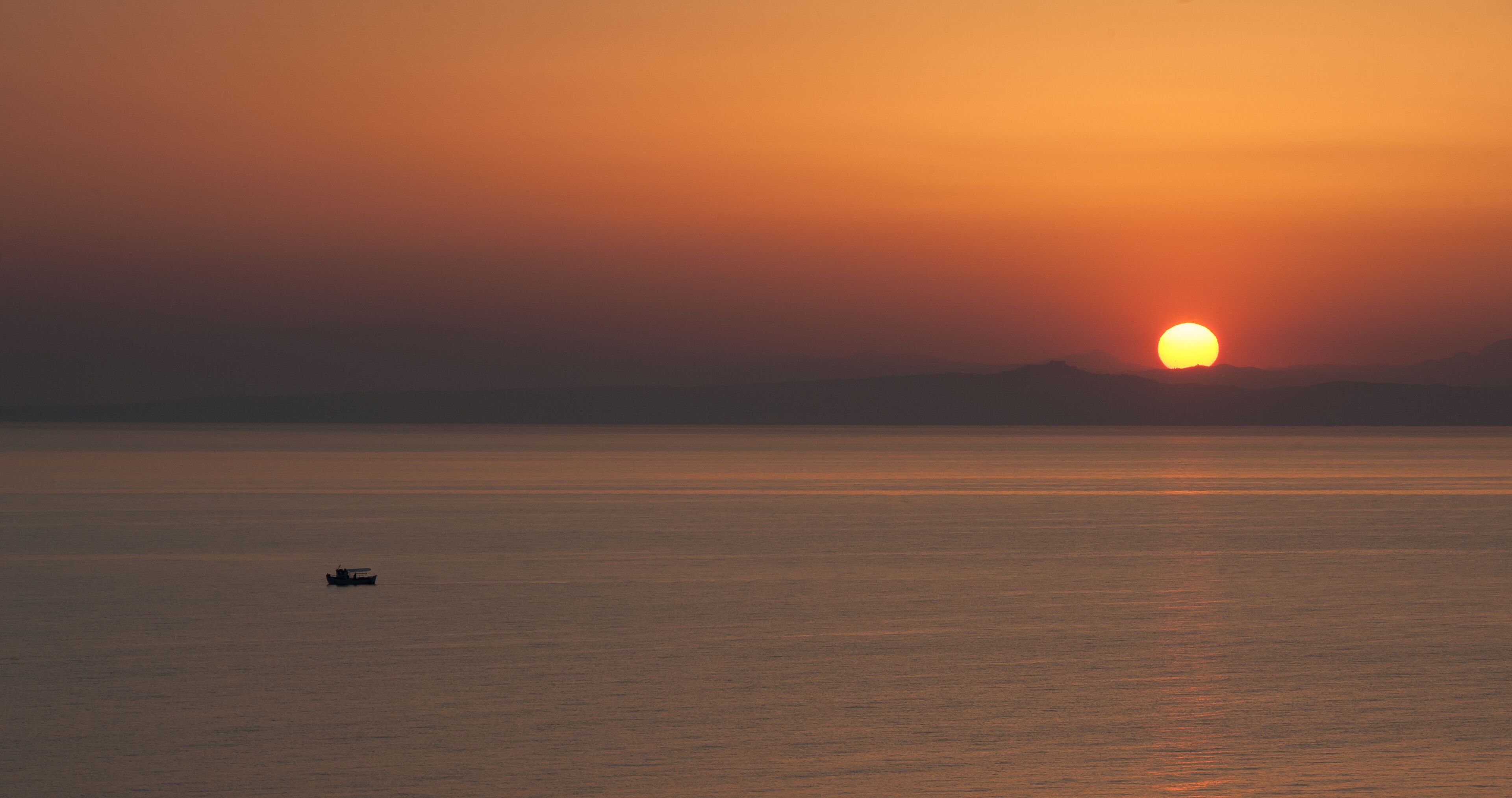 Atardecer sobre un mar tranquilo con un barco a lo lejos.
