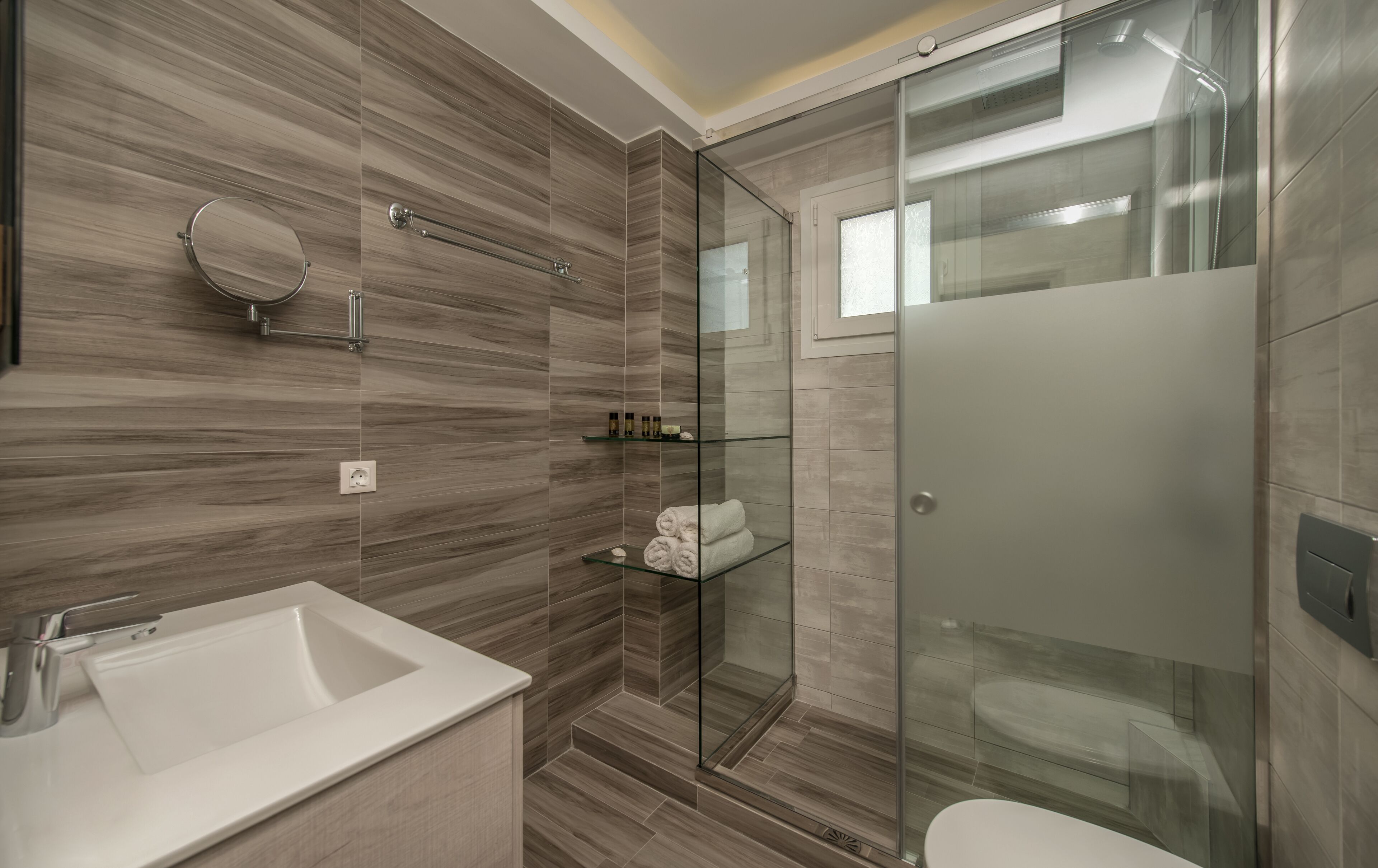 Un bagno moderno con doccia vetrata, lavandino bianco e porta doccia in vetro.