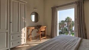 Un dormitori amb llit, escriptori de fusta, una cadira, armari i un balcó amb cortines.