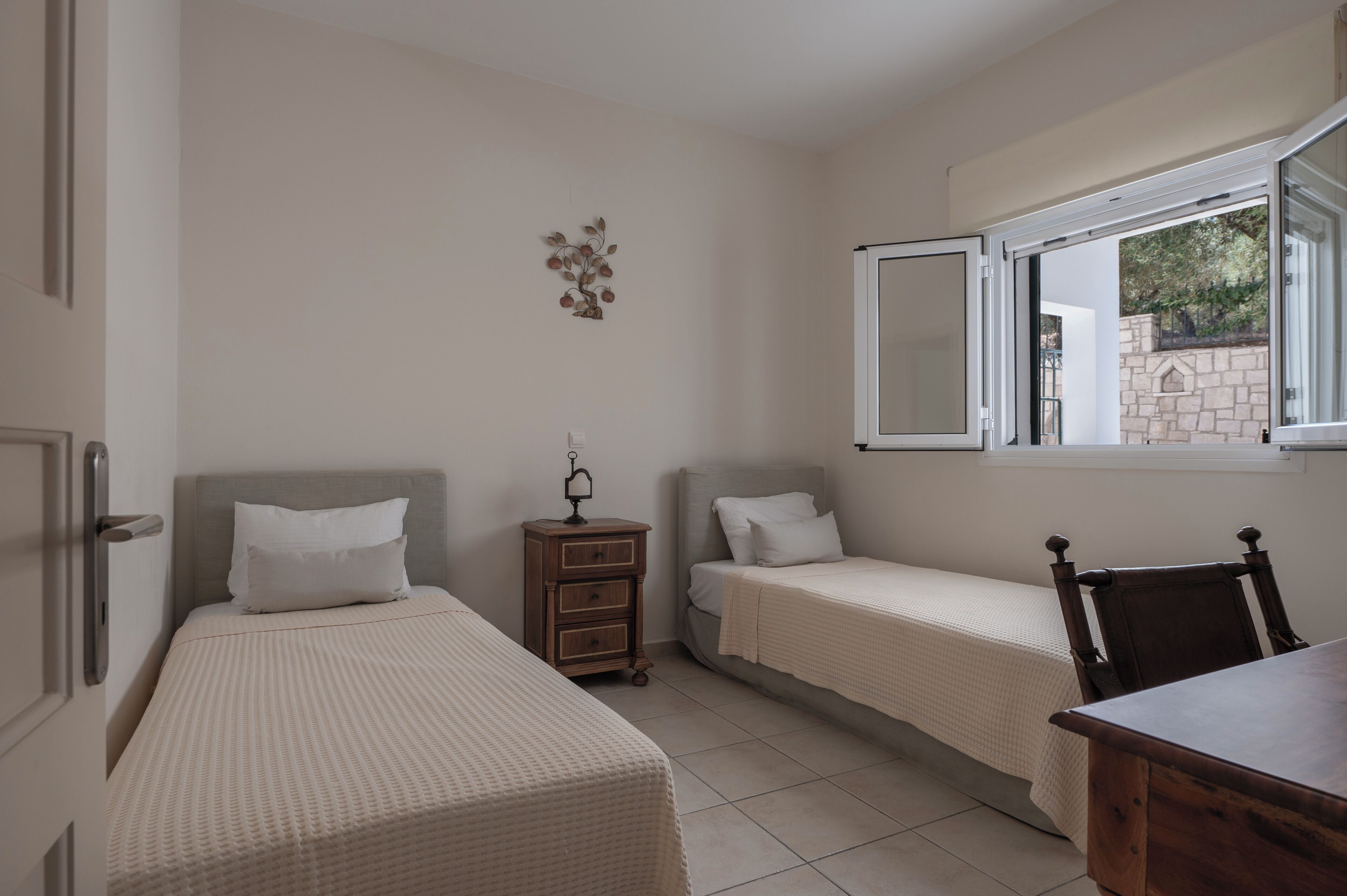 Una camera da letto con due letti singoli, un comodino in legno, una sedia e una finestra con persiana aperta.