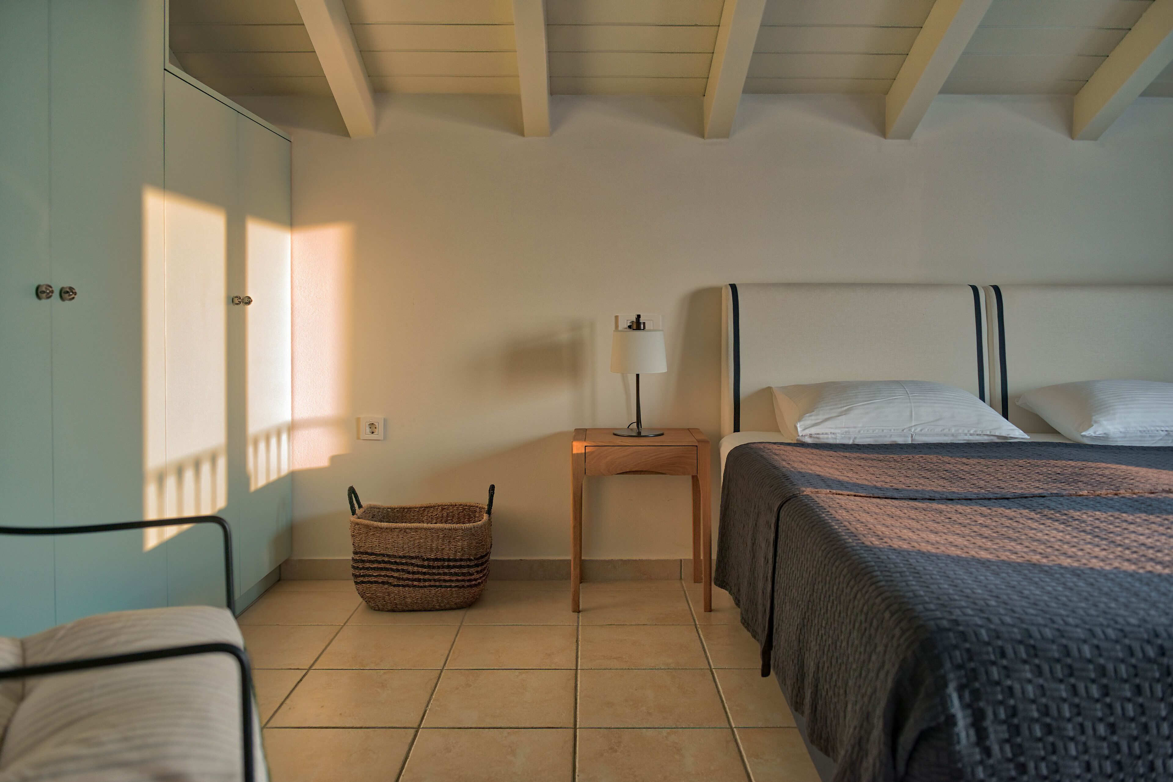A bedroom with a bed, a bedside table with a lamp, a wicker basket, and a wardrobe.