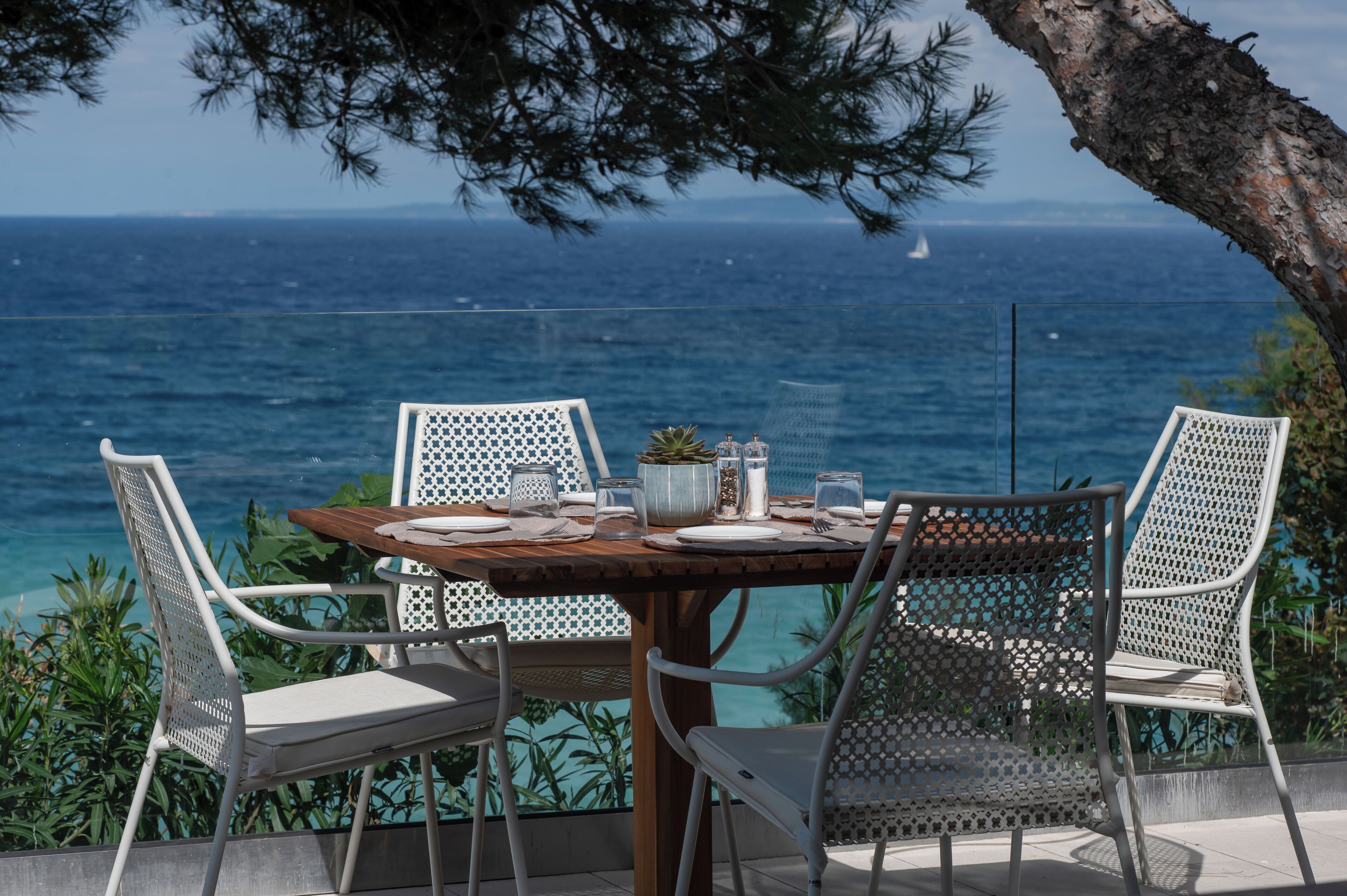 Une table dressée à l’extérieur, avec des chaises, une vue sur la mer et un bateau à l’horizon.