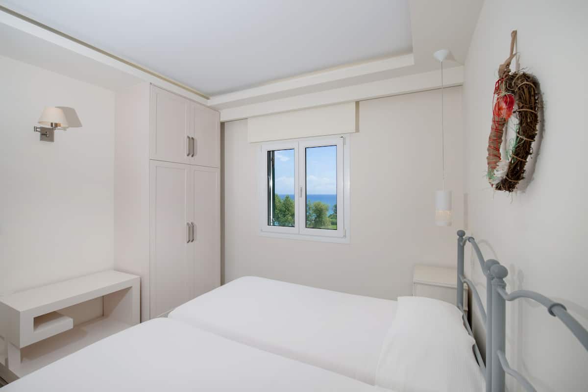 A bedroom with a bed, a wardrobe, a bedside table, a window with a view, and a wall-mounted light fixture.