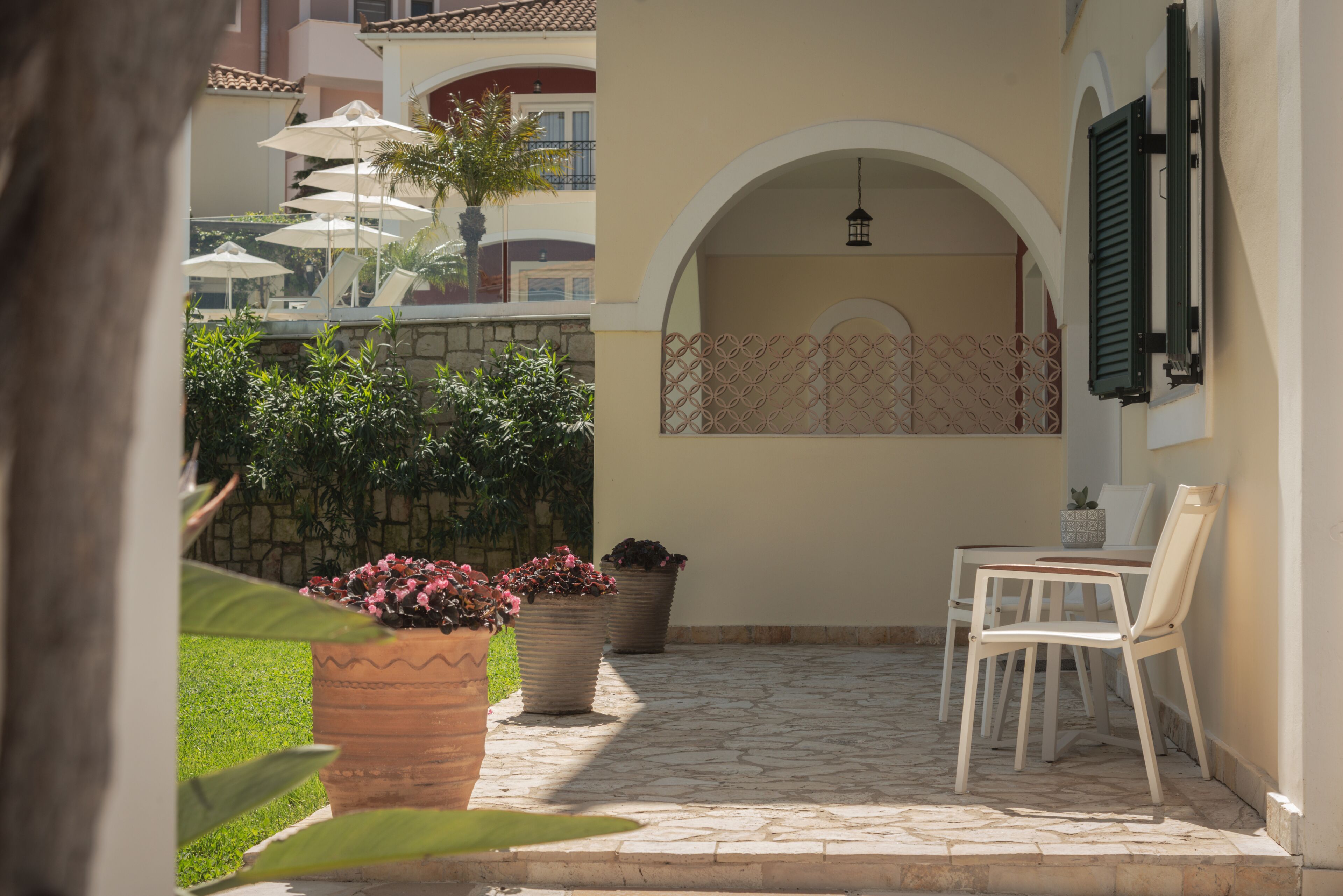Un patio con mesa y sillas, plantas en macetas y sombrillas.