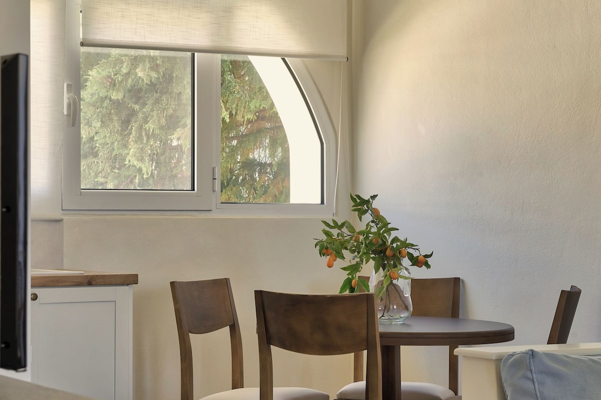 A modern dining area with a round table, wooden chairs, and a hanging light fixture.