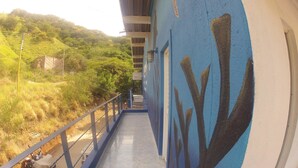 Un couloir avec un mur bleu orné d’une fresque représentant une tortue de mer, une rambarde en métal et une vue sur un paysage vallonné à la végétation clairsemée.