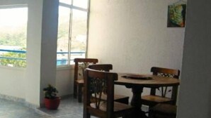 Une pièce avec une table ronde et quatre chaises, une plante en pot et une fenêtre donnant sur un paysage verdoyant.