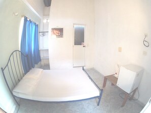 A small, single-bed room with a metal frame, a wooden nightstand, a white cabinet, and a door with a glass panel. - Hotel Tayrona Dive Center (Santa Marta)
