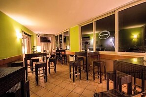 A restaurant with wicker furniture and a tiled floor, large windows, and a green wall.
