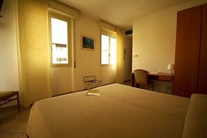 A hotel room with a bed, a desk, a chair, and a window.
