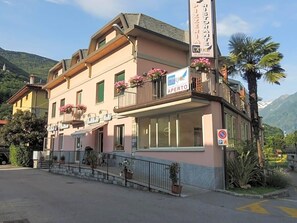 A two-story building with a restaurant sign, a visible entrance, and a mountain backdrop. - Albergo Lario (Gera Lario)
