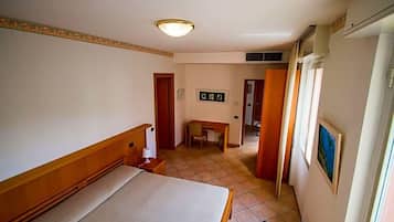 A hotel room with a bed, a desk, and a chair. There is a door leading to another room and a window with curtains.