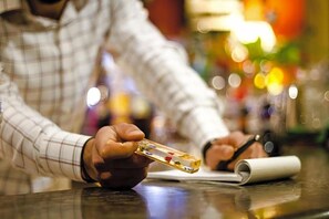 Une personne tient un objet transparent orné de motifs colorés, peut-être une carte ou un pion de jeu, au-dessus d’une table sur laquelle se trouve une feuille de papier enroulée.