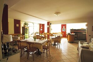 A dining area with multiple tables and chairs, a kitchen area, and a view of the outside.