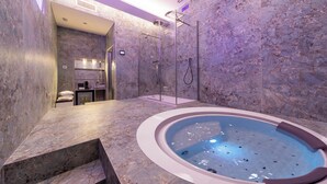 Un baño moderno con piso de mármol, un jacuzzi circular y zona de ducha con paredes de vidrio.