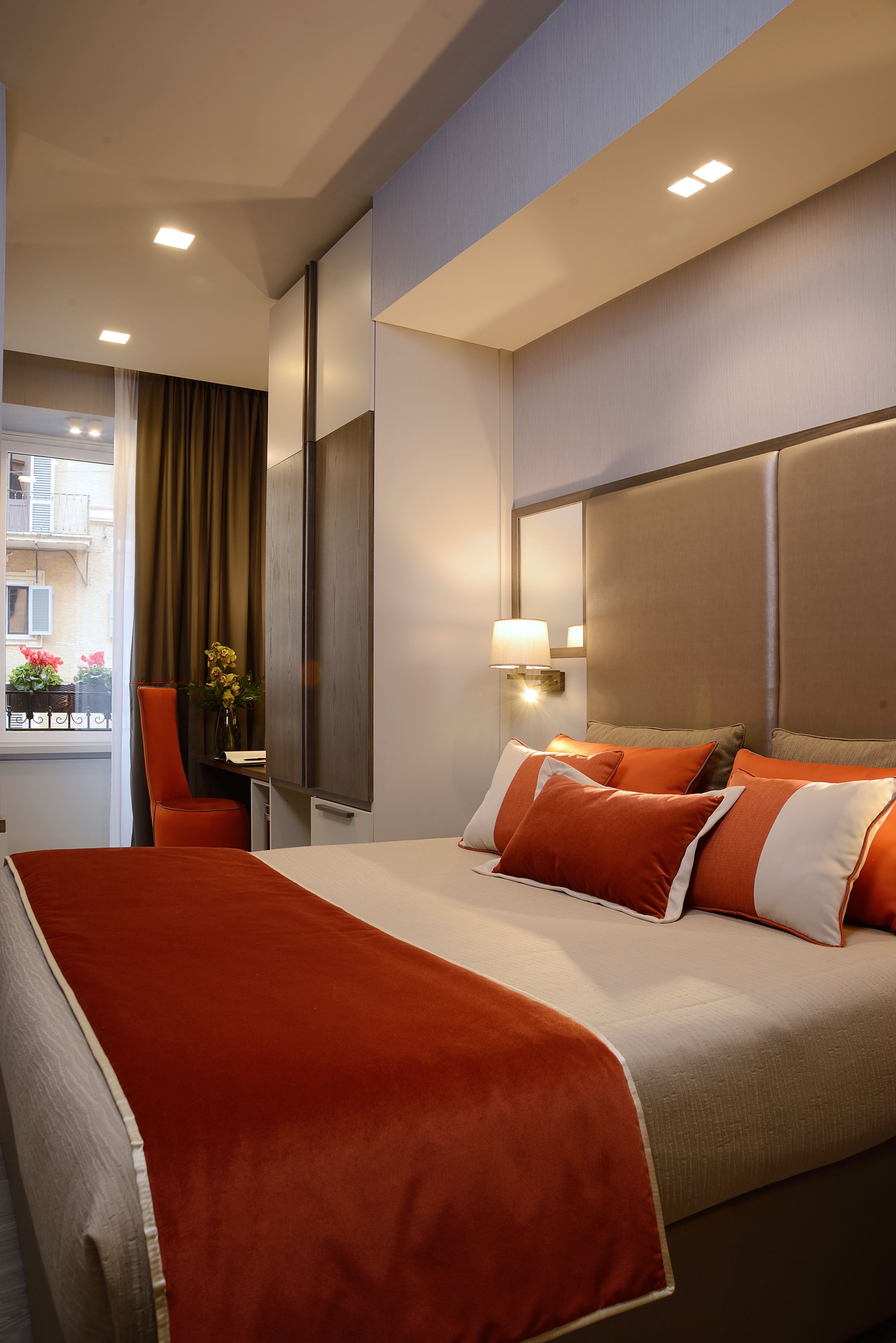Une chambre d’hôtel avec un grand lit, un bureau avec une lampe, une chaise et une fenêtre avec des rideaux.