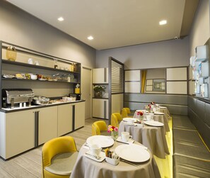 A dining area with tables set for service, a buffet station, and a seating area with yellow chairs. - San Carlo Suite (Rome)