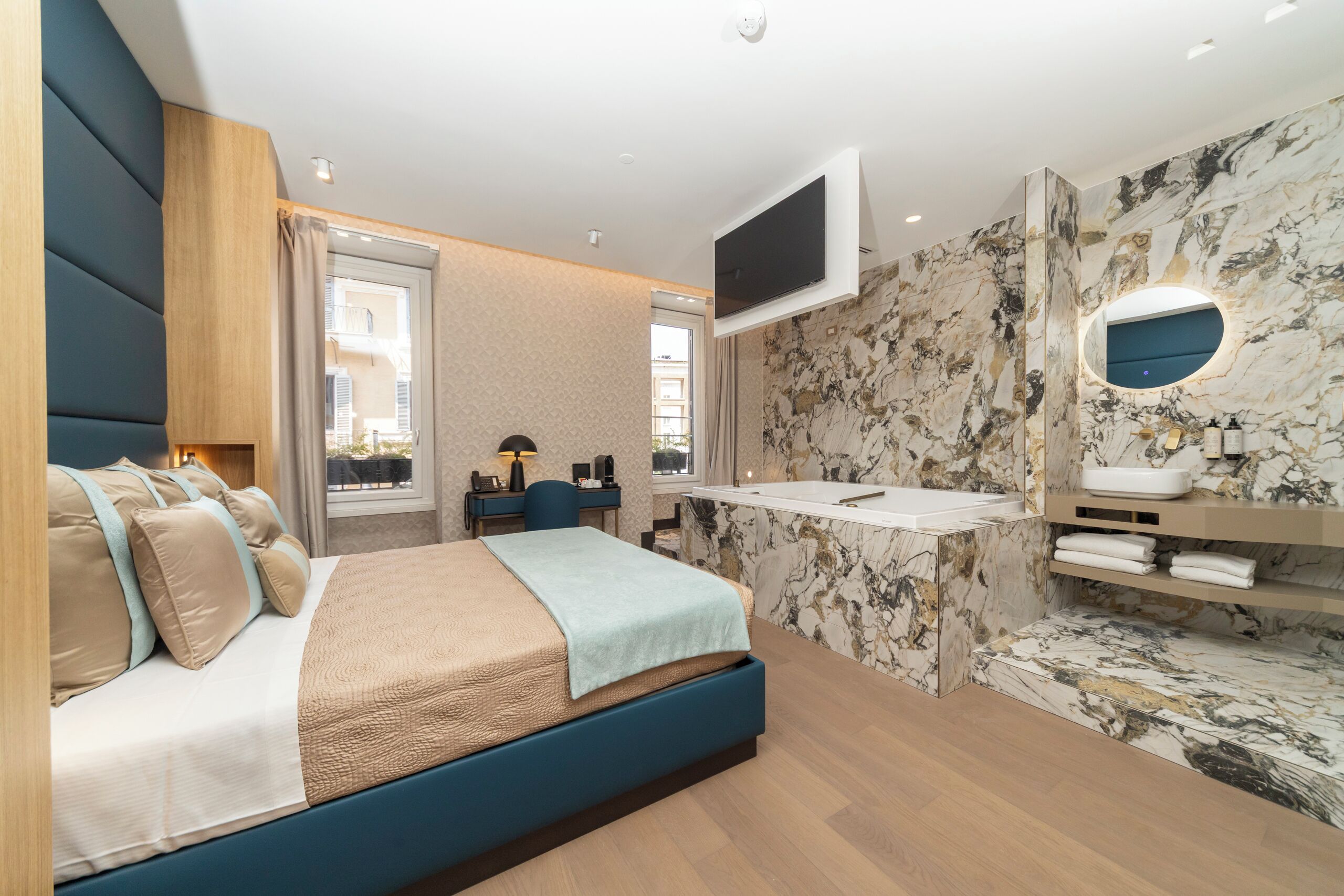 A modern bedroom with a large bed, a desk, a TV, and a bathroom with a marble wall.