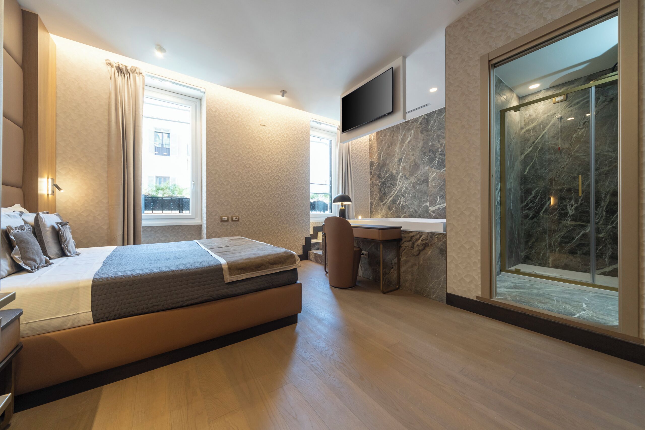 Ein modernes Hotelzimmer mit einem großen Bett, einem Badezimmer mit Glasdusche, einem Flachbildfernseher und einem großen Fenster mit Blick ins Freie.